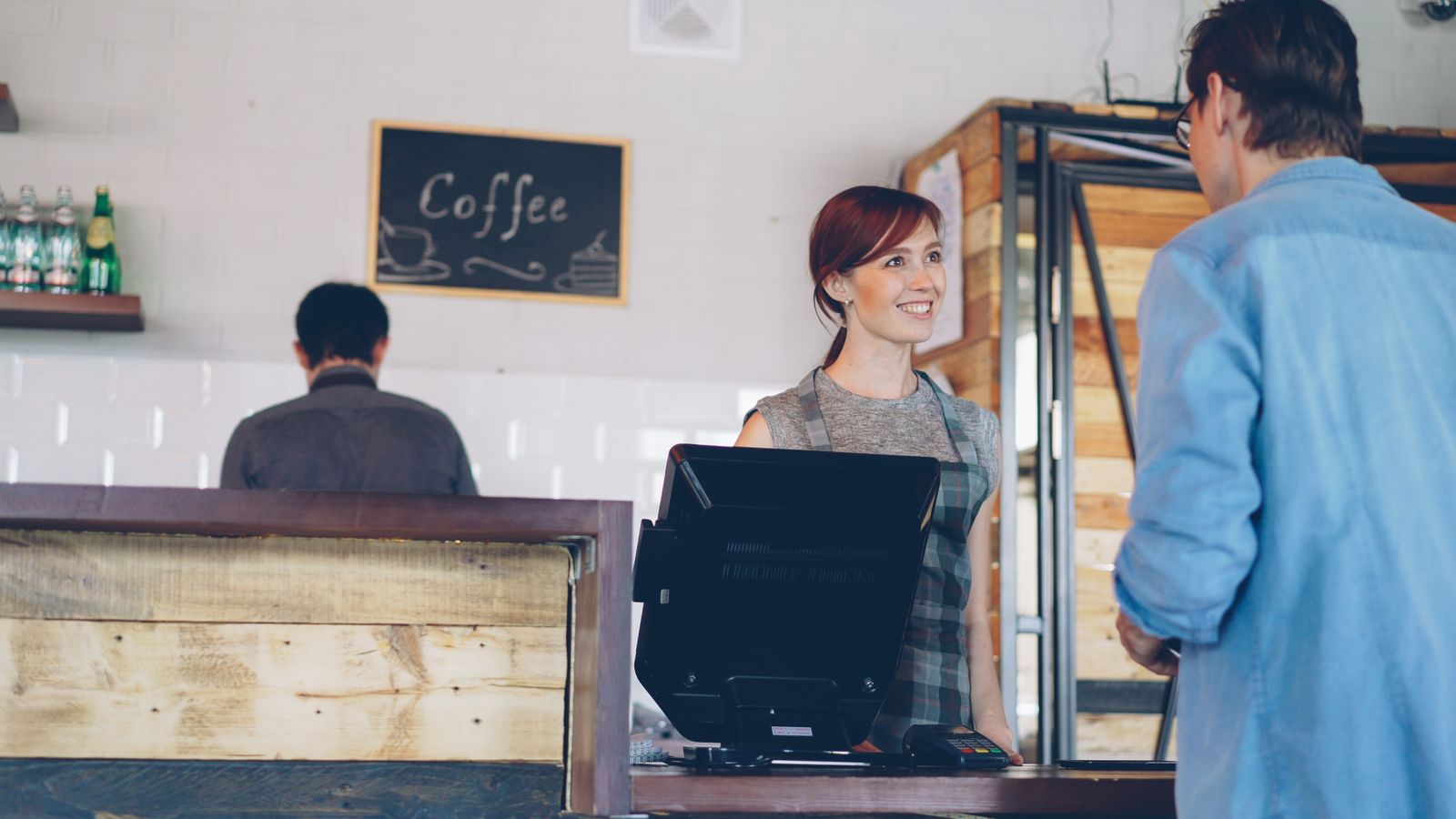 A barista smiling at a customer at the café till