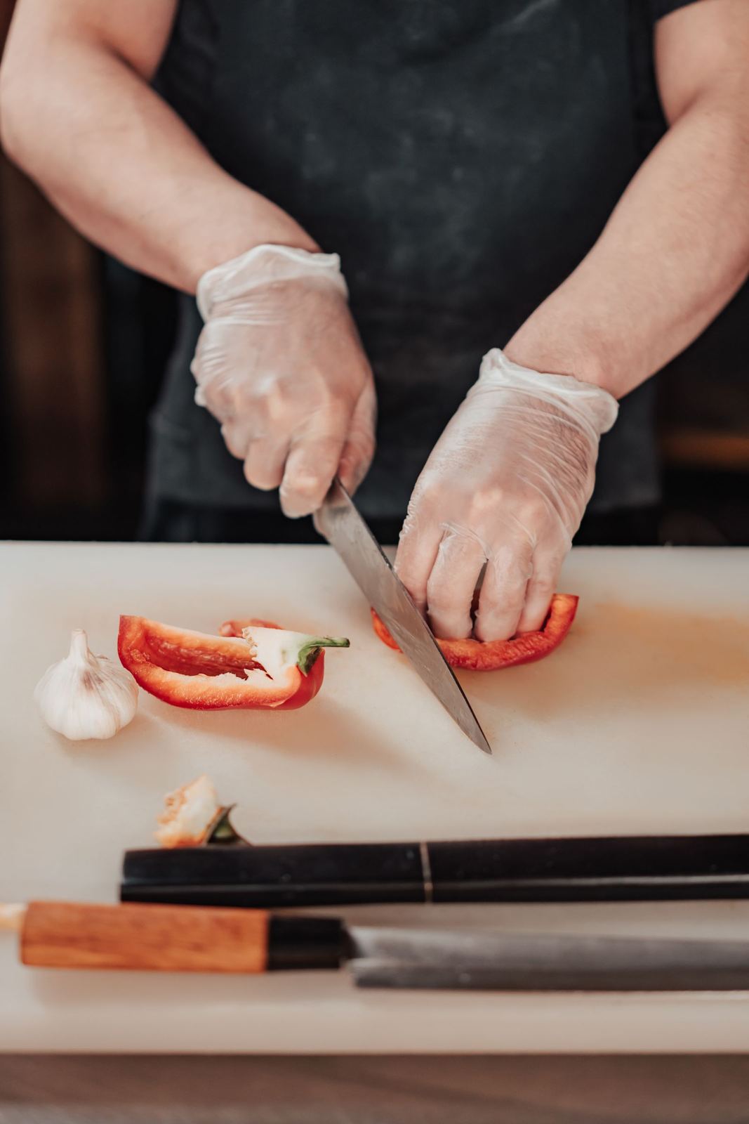 Gloved hands slicing a pepper on a clean board