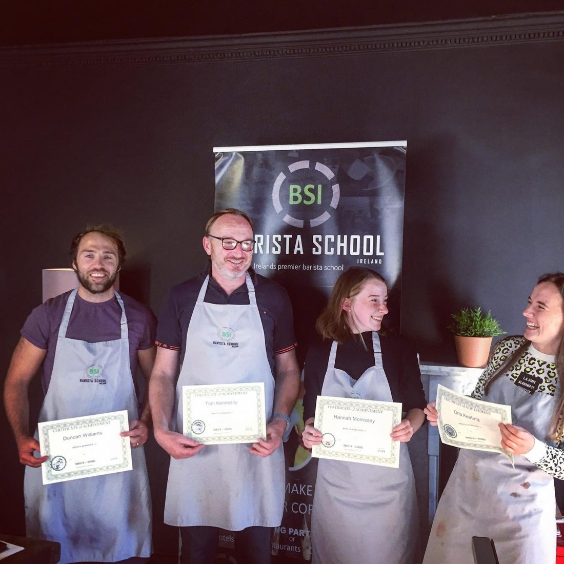 Four graduates in aprons holding their Barista School Ireland certificates