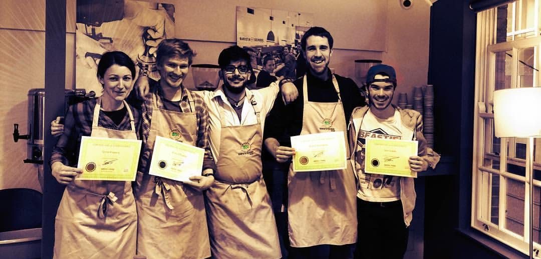 Five graduates in aprons holding up their certificates